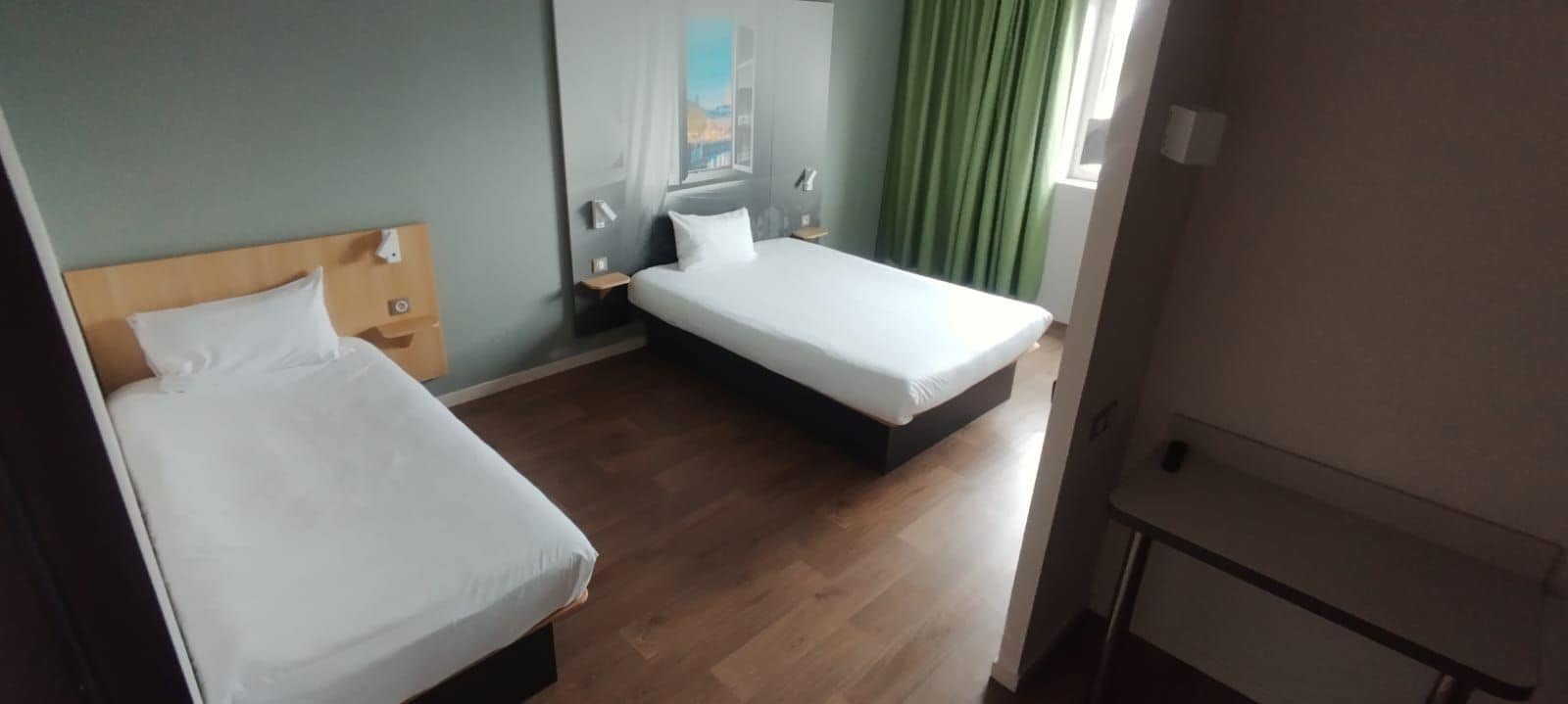 A hotel room with two beds, a wooden headboard, a nightstand, and a painting on the wall.