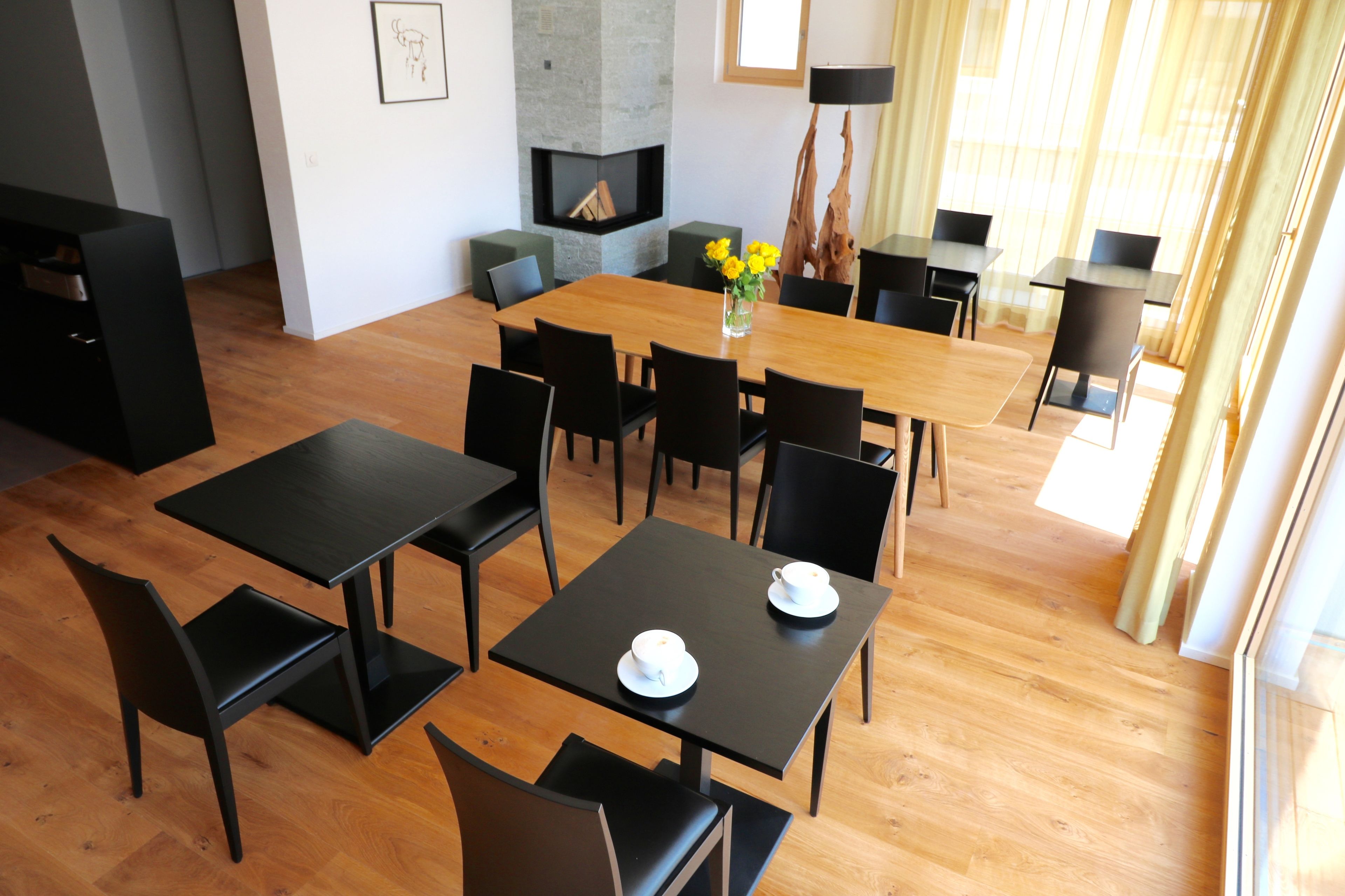 Un comedor moderno con una mesa de madera y sillas negras, una chimenea y vistas al exterior.