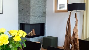 Un espace de salle à manger moderne avec une table en bois, des chaises, un vase de roses jaunes, un mur d’accent en pierre, une cheminée et une grande sculpture en bois.