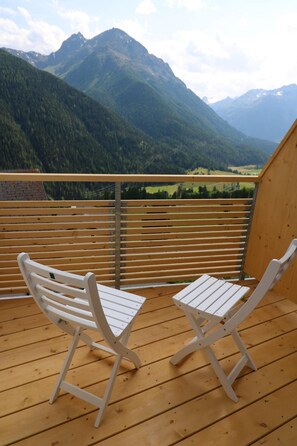 Two white chairs on a wooden deck with a view of mountains.