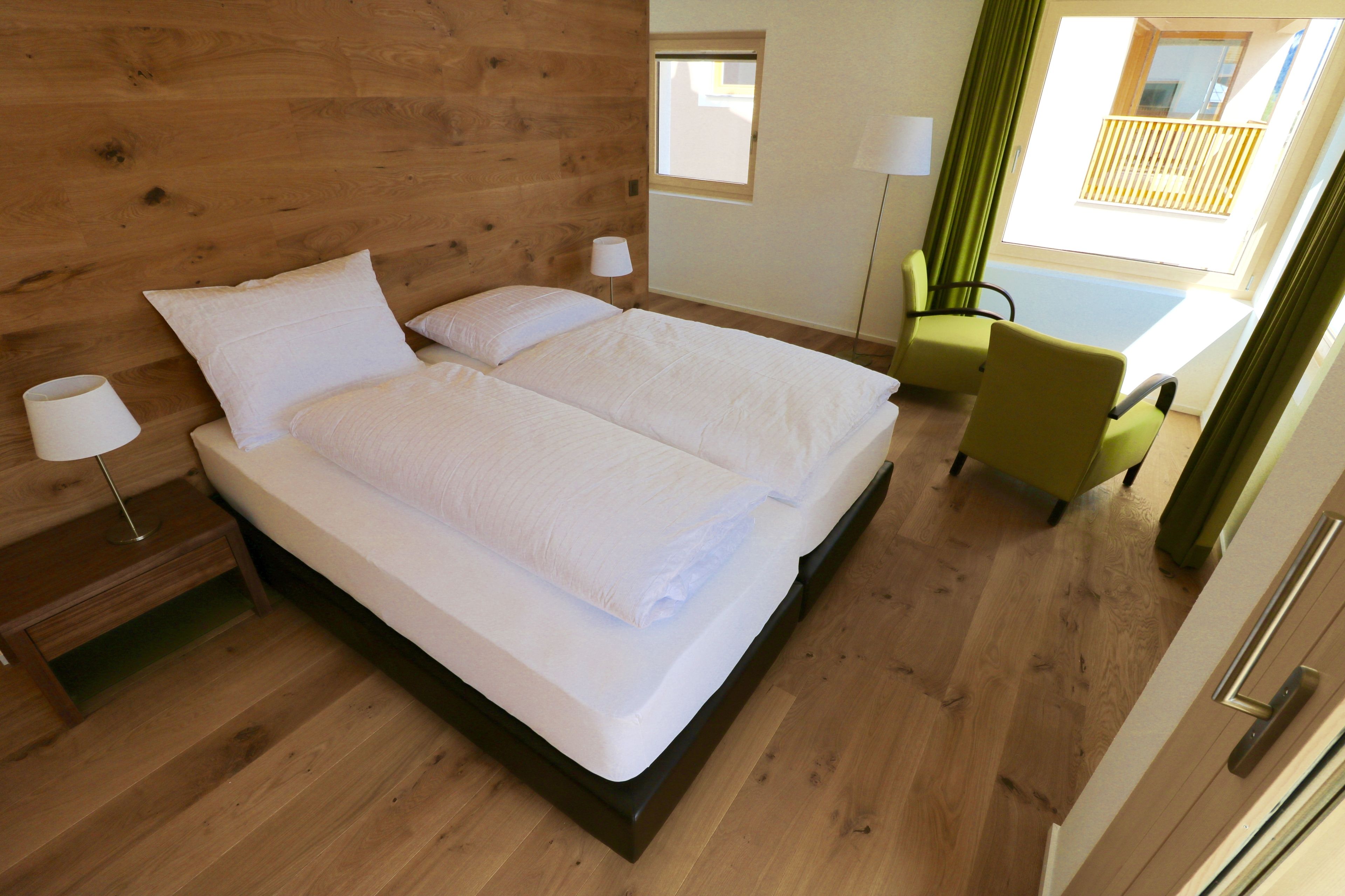 A double bed with white linens, a bedside table with a lamp, and a view of a balcony with a railing.