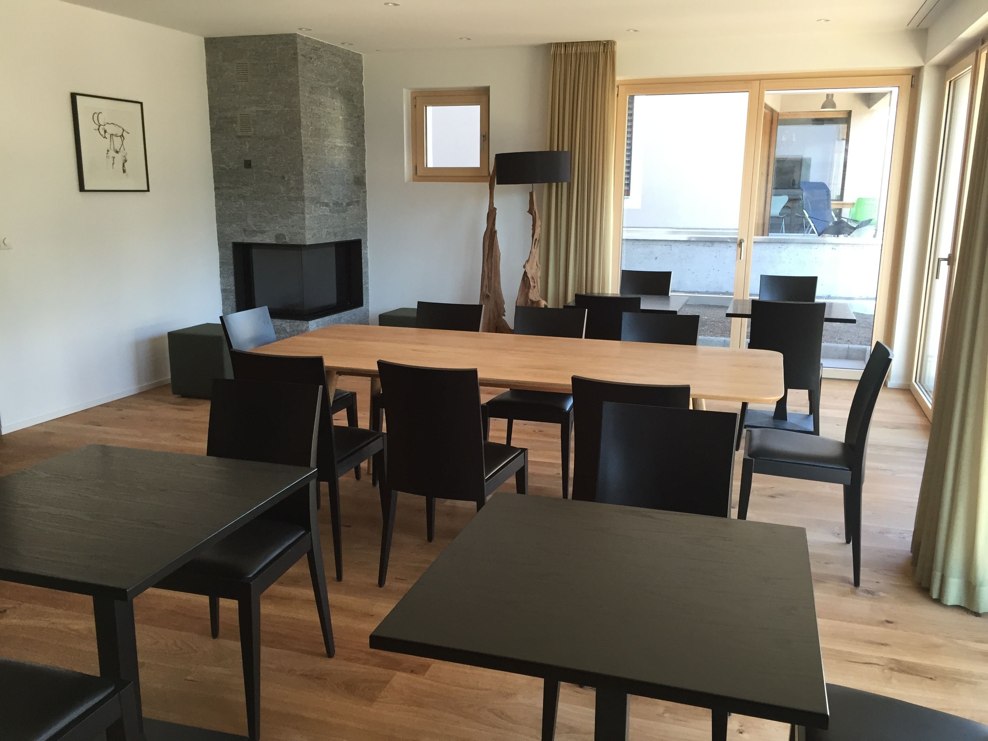 A modern dining area with a large wooden table and black chairs, a stone fireplace, and a view of the outdoors through large windows.