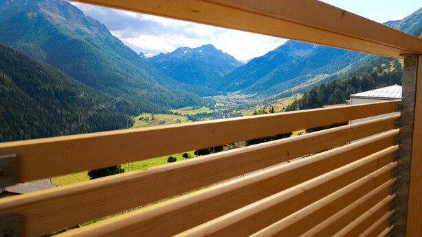 Un balcon en bois offrant une vue sur une vallée et des montagnes.