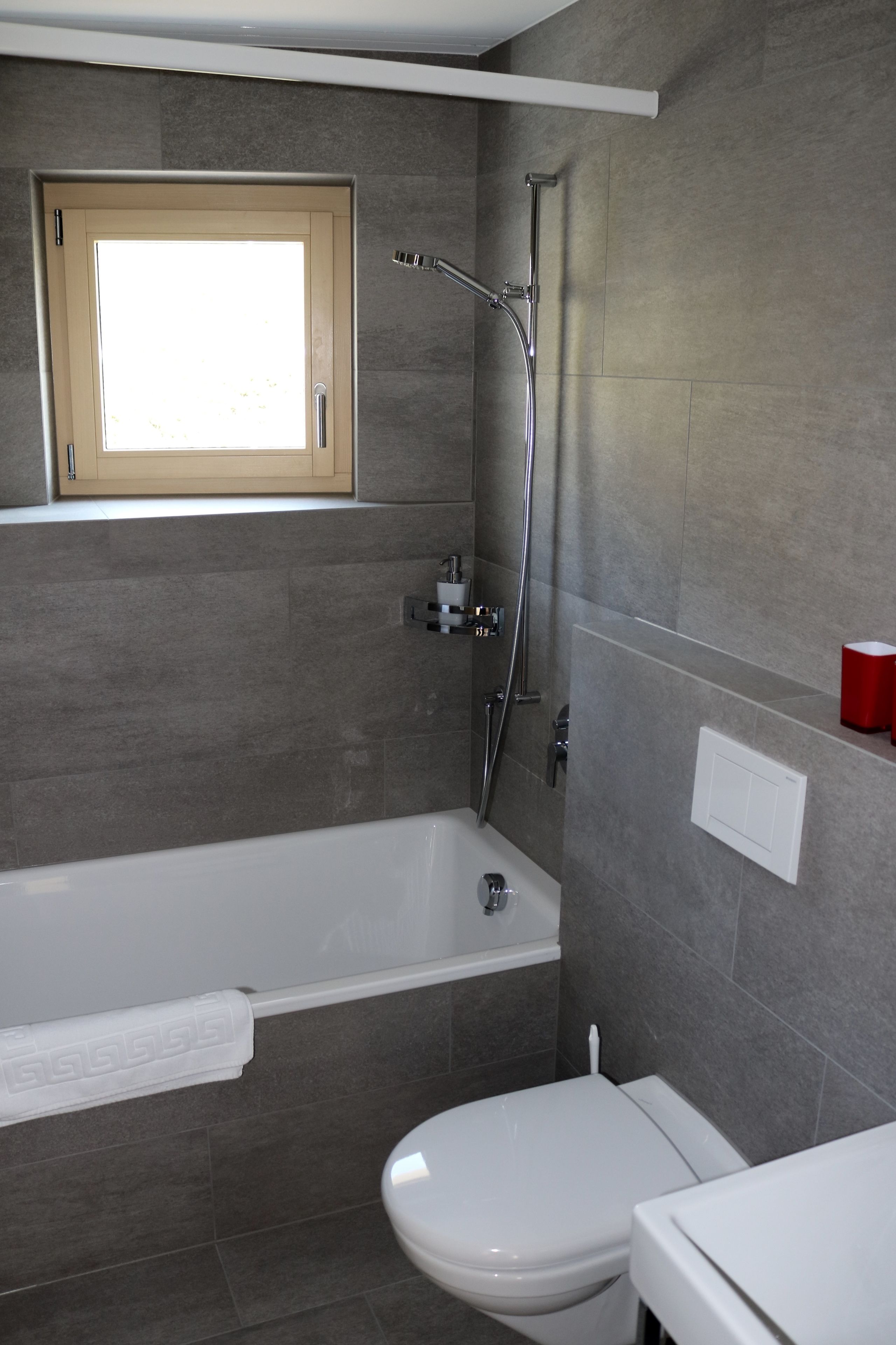 A modern bathroom with a bathtub, toilet, and a window above the sink.
