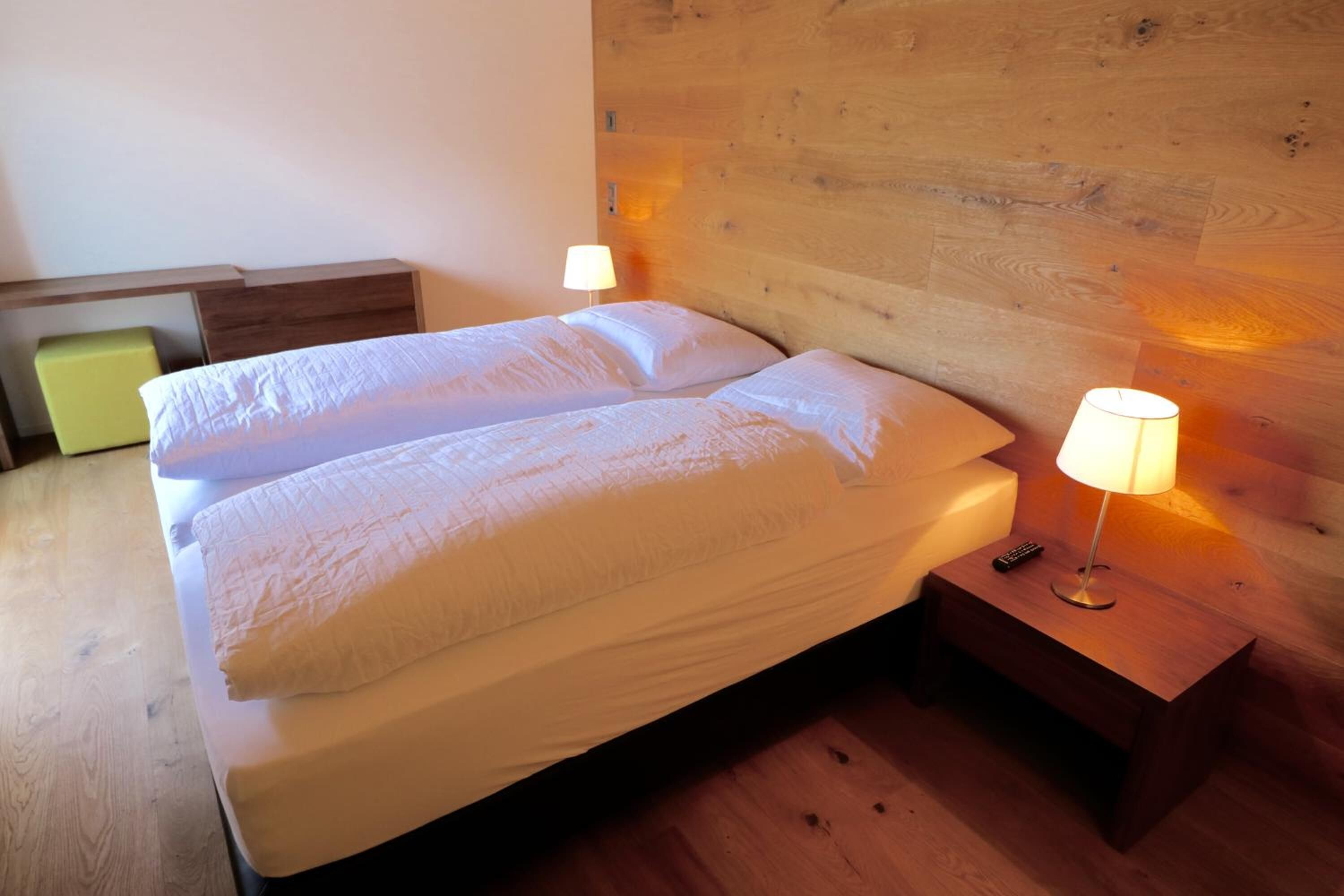 A neatly made bed with two pillows and a bedside table with a lamp and remote control.