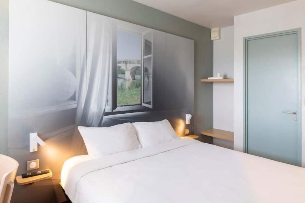 Une chambre d’hôtel comprenant un lit, des tables de chevet, une commode, une fenêtre avec des rideaux, une porte et une étagère.