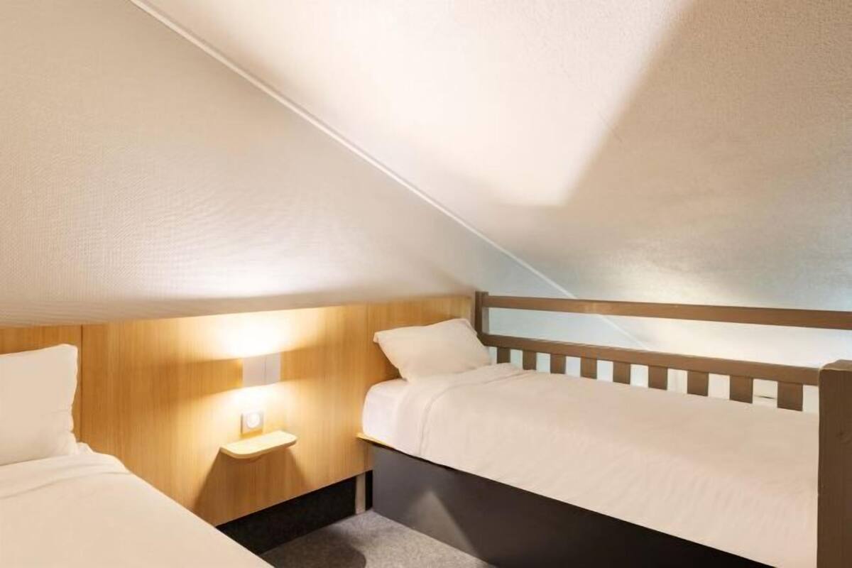 Une petite pièce bien éclairée, avec deux lits, une table de chevet et un plafond en pente.