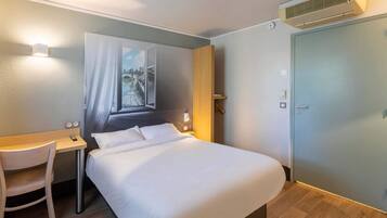 Una habitación de hotel con cama, escritorio, silla, un cuadro y una puerta.