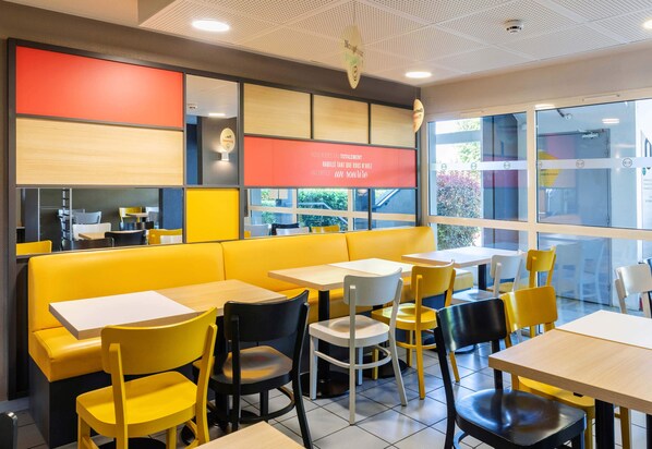Un interior de restaurante con asientos amarillos y blancos, un letrero rojo y ventanas amplias.