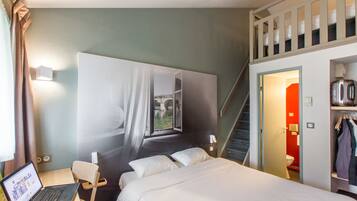 Habitación de hotel con cama, escritorio con computadora portátil, escalera y vistas al exterior.