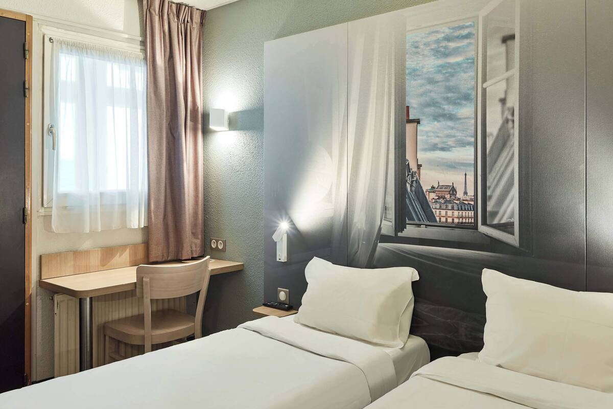 A hotel room with two beds, a desk, and a chair.