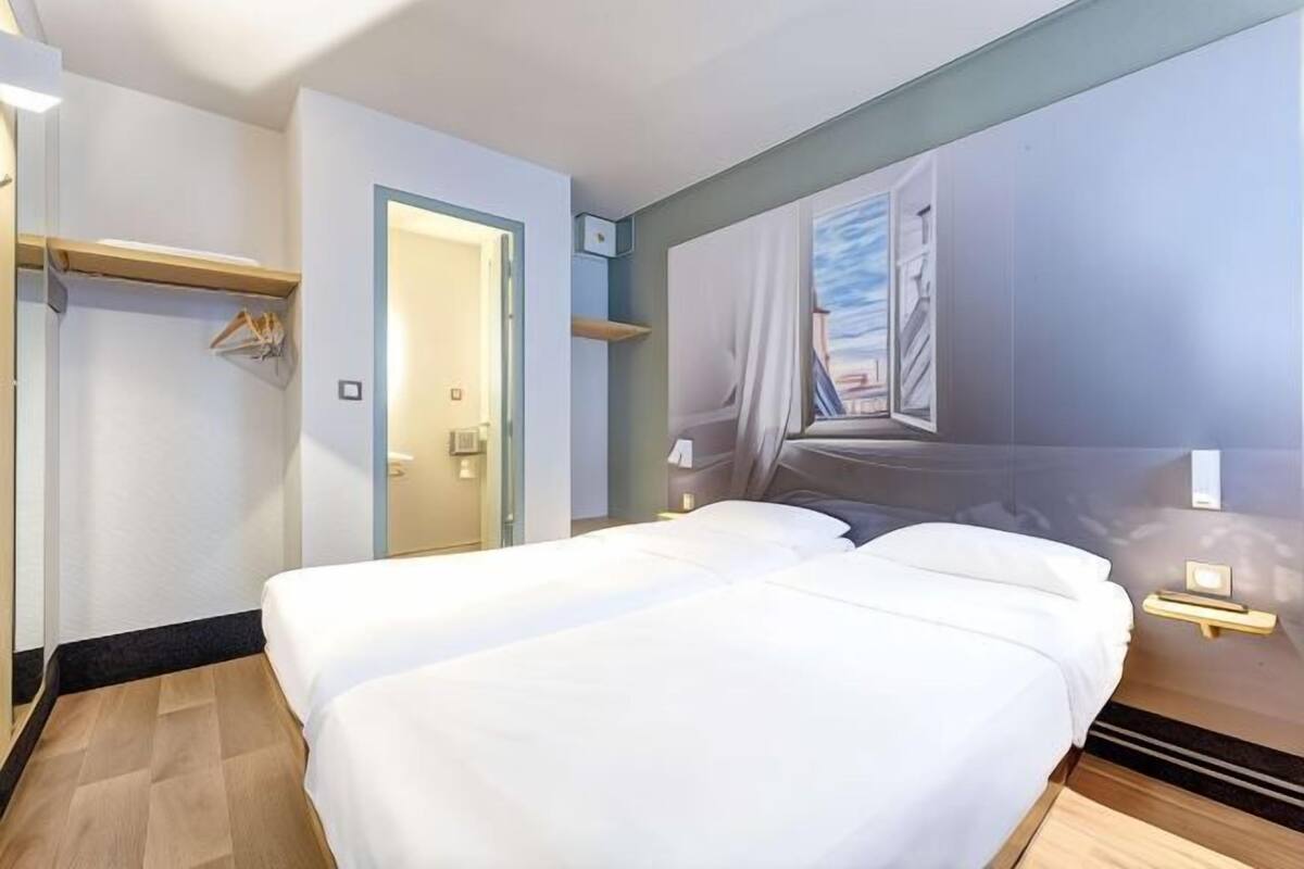 A hotel room with a bed, bedside tables, a wardrobe, and a door leading to another room.