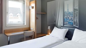 A hotel room with a bed, a desk, a chair, and a window with a cityscape view. - B&B HOTEL Paris Nord Villepinte (Villepinte)