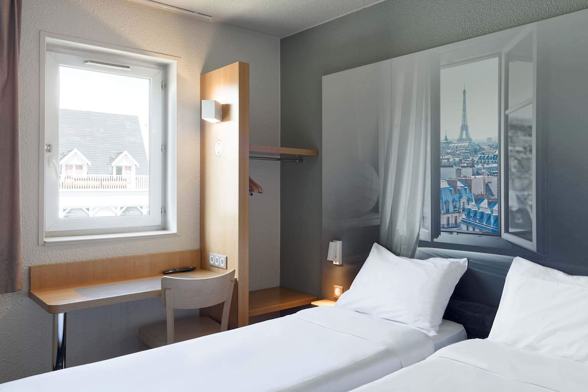 Een hotelkamer met een bed, een bureau, een stoel en een raam met uitzicht op de stad.