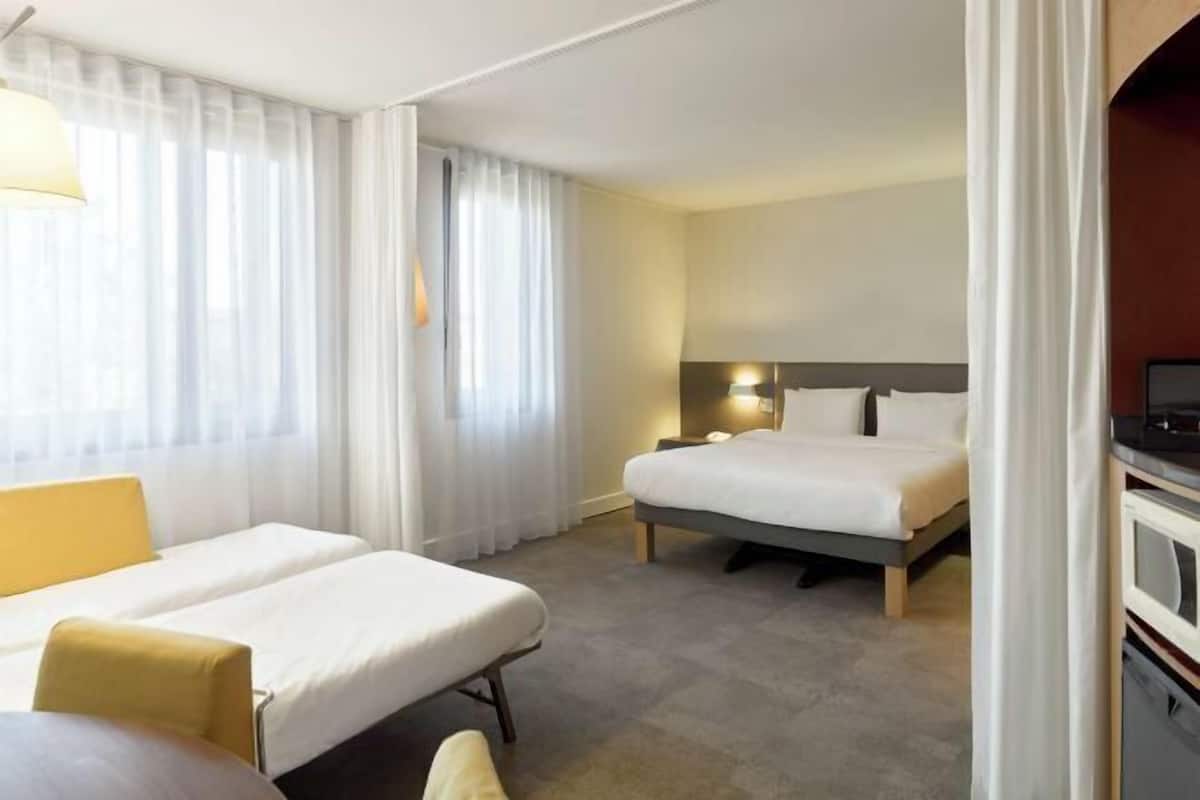 Hotelkamer met twee bedden, een bureau, een stoel, een televisie en een raam met gordijnen.