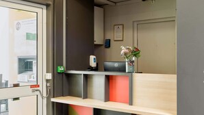 A reception desk with a computer, a vase with flowers, and a sign indicating a self-service kiosk. - B&B HOTEL Paris Nord Villepinte (Villepinte)
