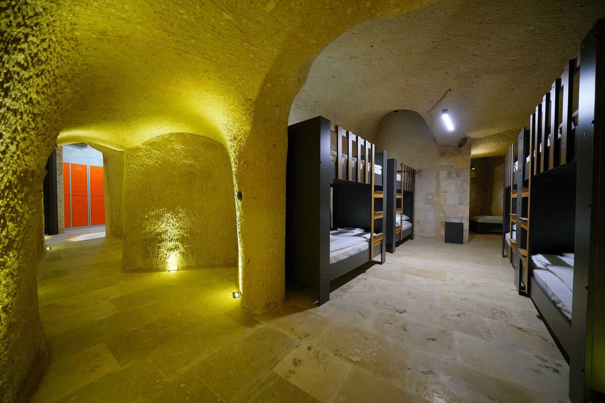 Habitación de hotel subterránea con literas, paredes de piedra y una cálida luz amarilla.