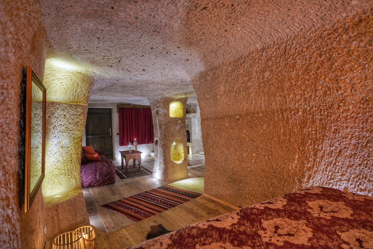 Una habitación con techo texturizado, suelo de madera, cortina roja y una pequeña mesa con lámpara.