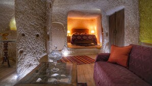 Quarto aconchegante com parede de pedra, cama com cabeceira de madeira, mesa de centro de vidro e sofá vermelho.