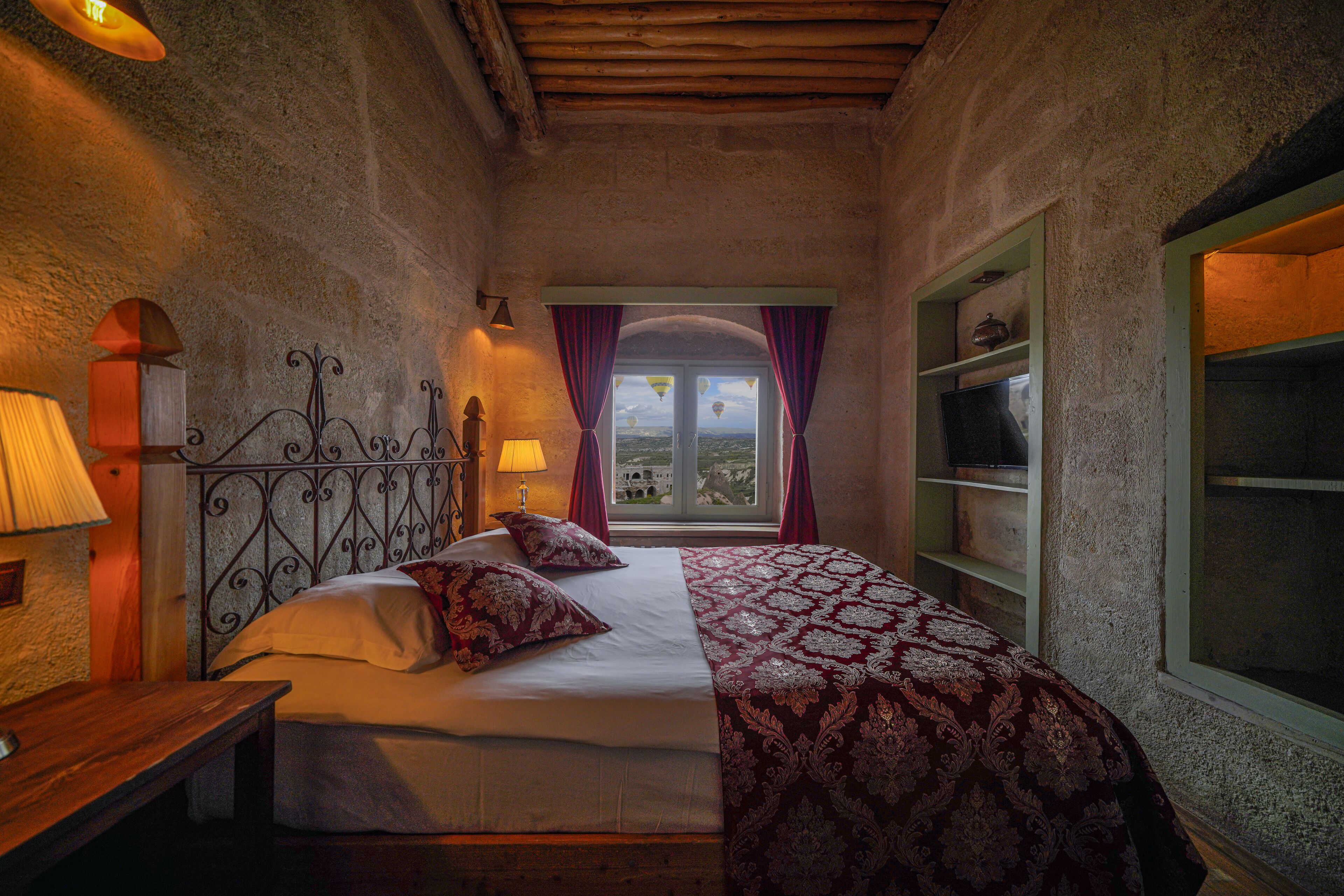 A bedroom with a bed, a nightstand, a lamp, a window with curtains, and a shelf with a decorative item.