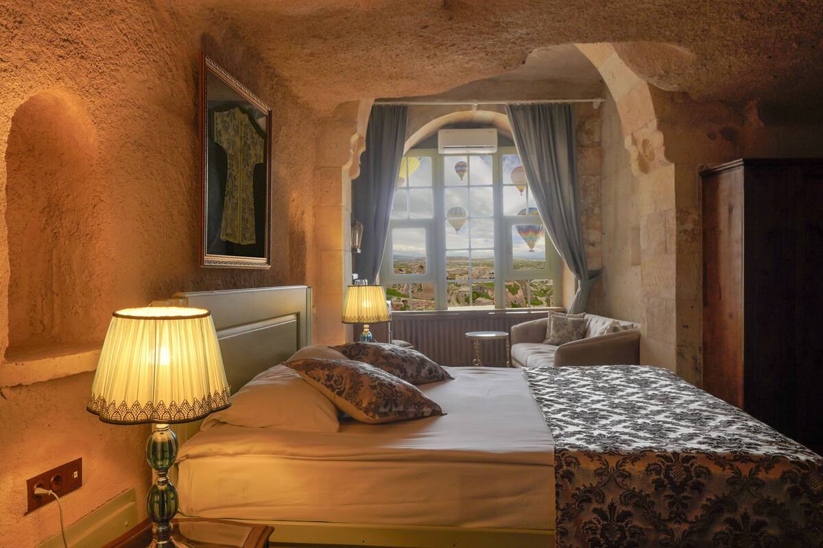 Una habitación con cama, lámpara, ventana con cortinas y vistas al exterior.