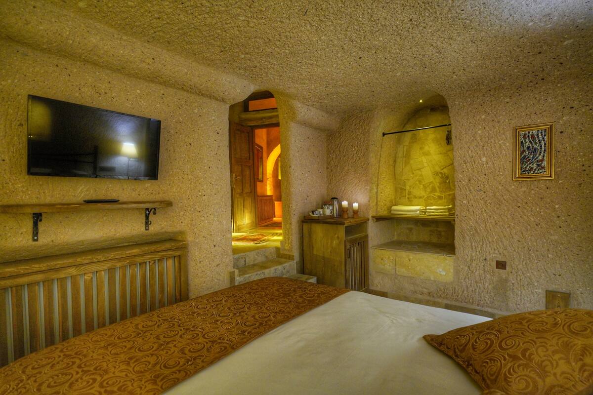 Habitación de hotel con una cama, televisión montada en la pared, un armario de madera y una mesita con velas.