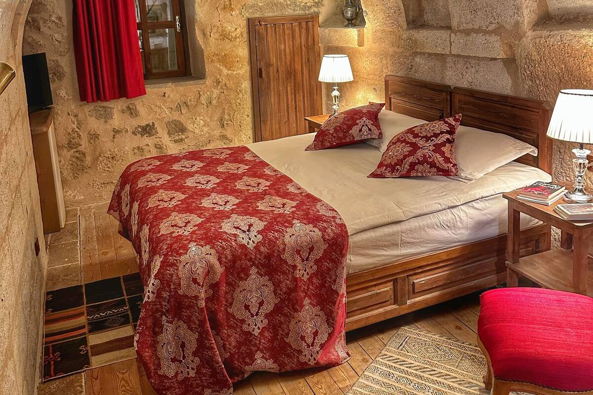 Un dormitorio acogedor con techo abovedado de piedra, una cama de madera, un sillón tapizado en rojo y una alfombra estampada.