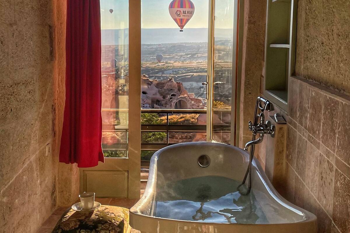 Un baño con una bañera grande, un taburete de madera y vistas de un globo aerostático sobre un paisaje.