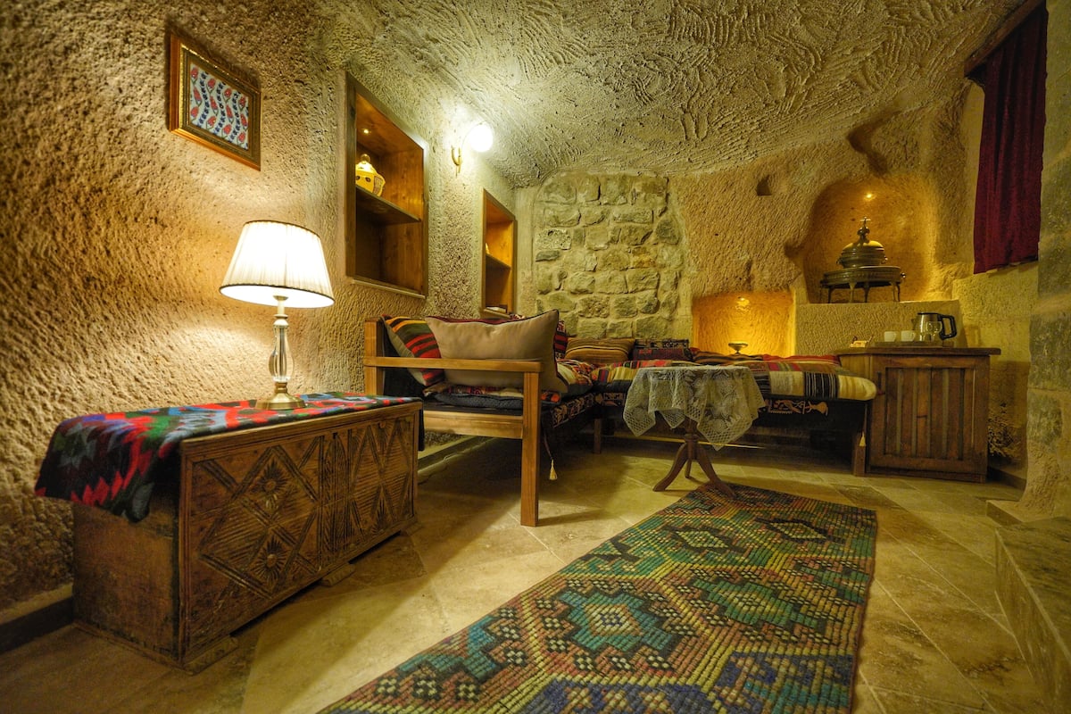 Una habitación acogedora con pared de piedra, un armario de madera, una mesa con lámpara y una alfombra estampada.