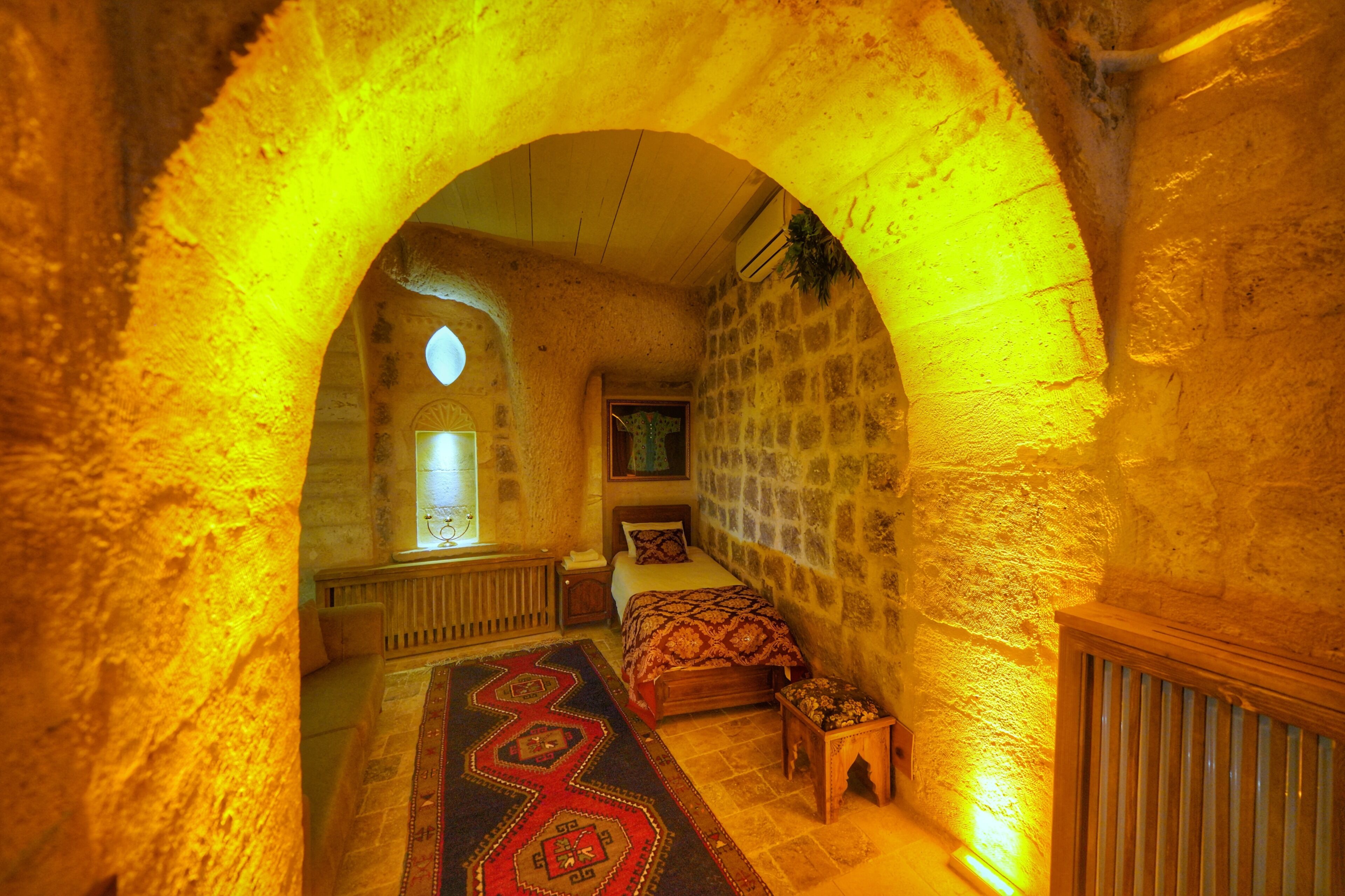 A narrow, stone-walled room with a bed, a small table, and a radiator.