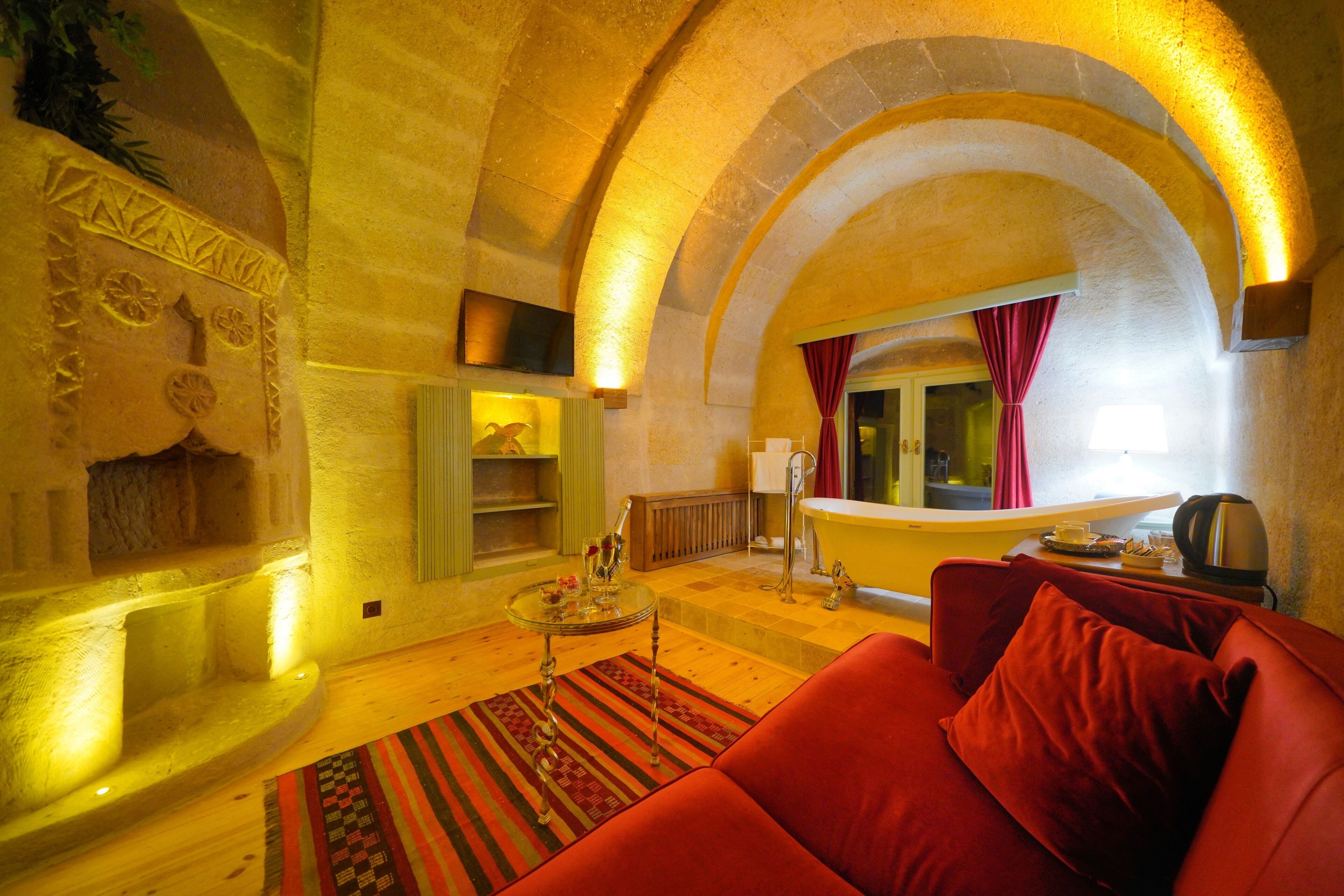 A cozy living room with a red sofa, a small table with drinks, a bathtub, and a stone fireplace.