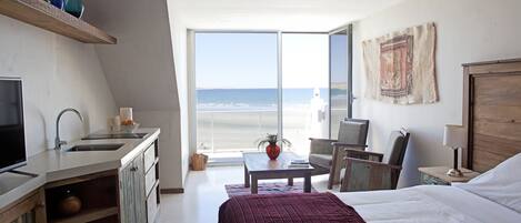 Un dormitorio con una cama grande, un escritorio, una silla, un televisor y vistas a la playa.