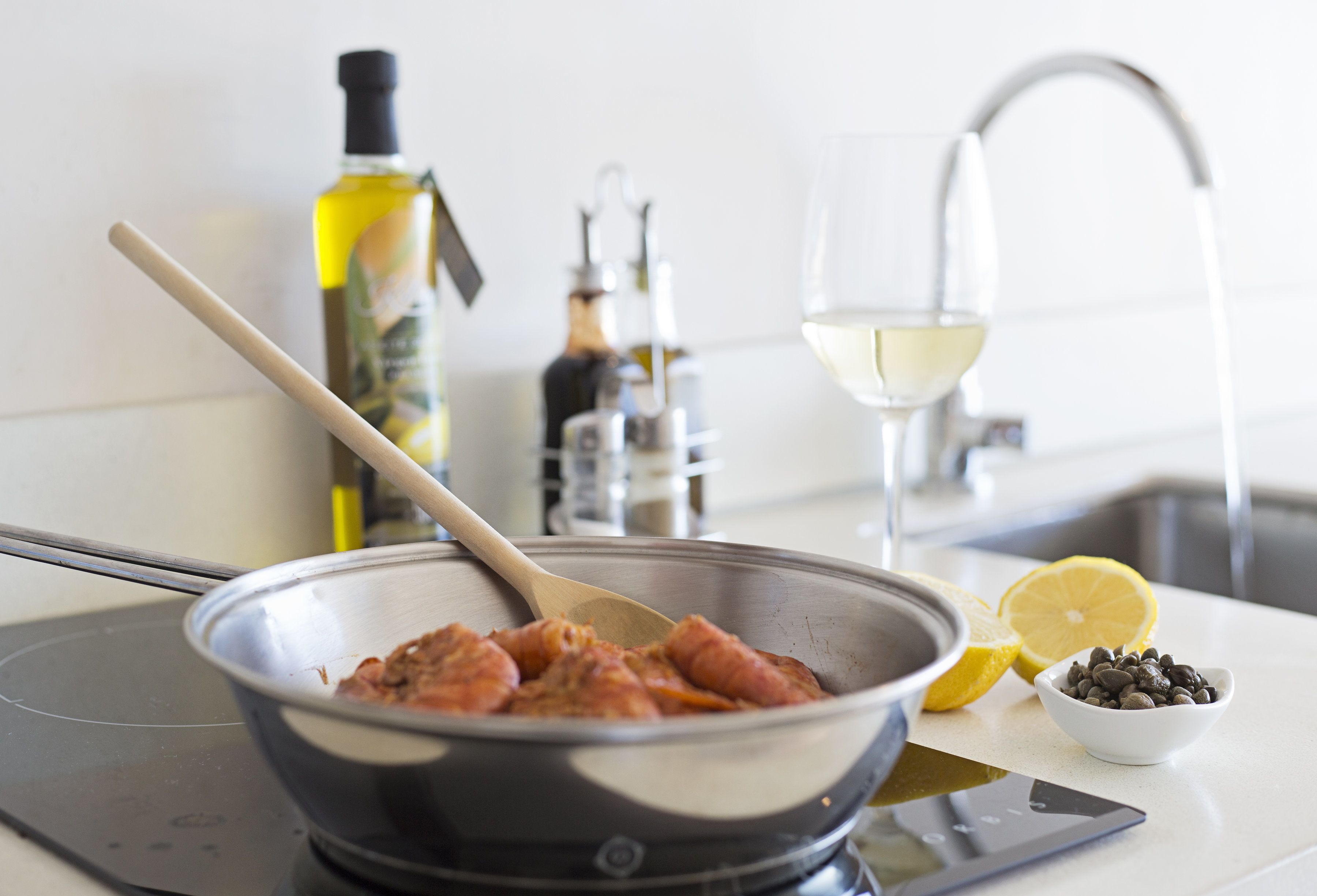 A kitchen counter with a frying pan, a wooden spoon, a bowl of chocolate chips, a lemon, and a bottle of olive oil.