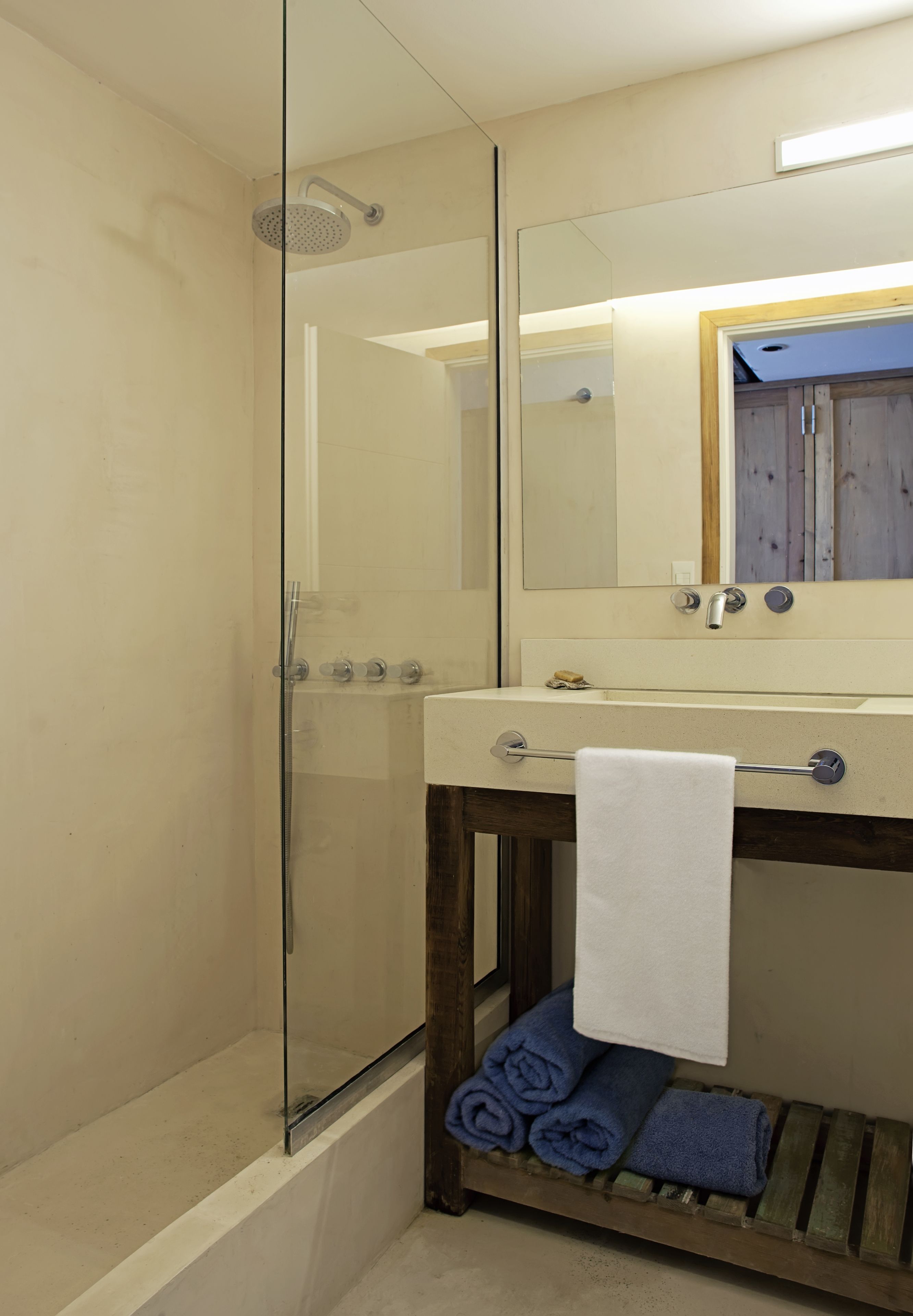 Un baño con ducha de vidrio, lavamanos con espejo y toallero con toallas dobladas.