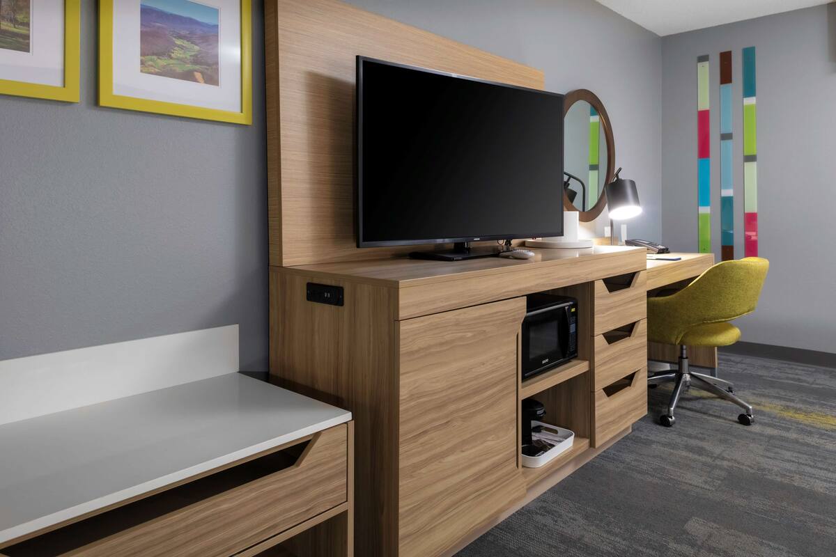 A modern office space with a wooden desk, a flat-screen TV, a desk lamp, a yellow office chair, and a colorful abstract wall art piece.