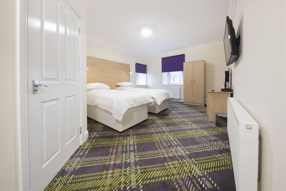 A hotel room with two beds, a wardrobe, a television, and a patterned carpet.