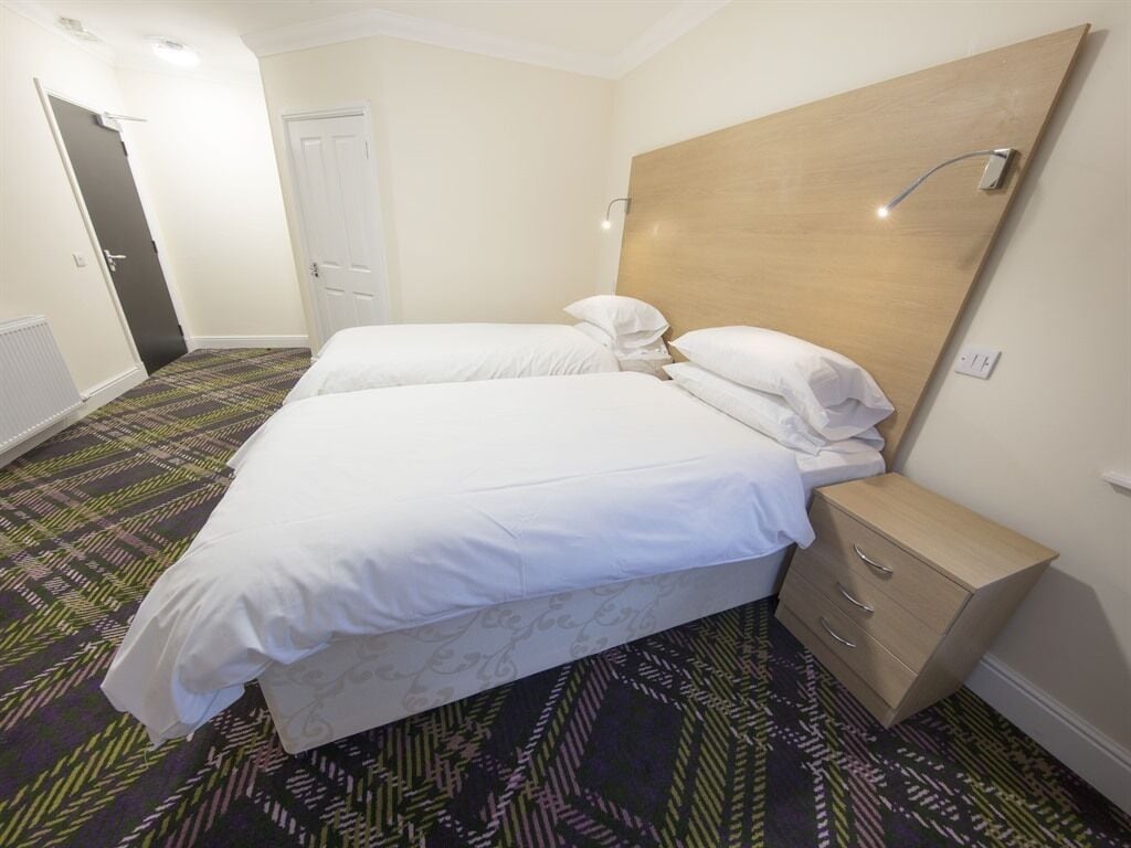 Habitación de hotel con una cama grande, una mesita de noche, un armario y una alfombra estampada.