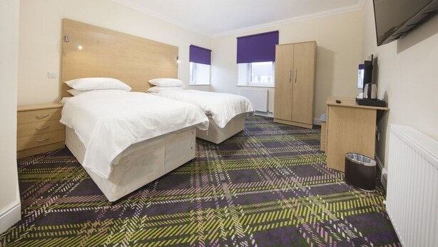 A hotel room with two beds, a wardrobe, a television, and a patterned carpet. - The Bay Horse (Hamilton)
