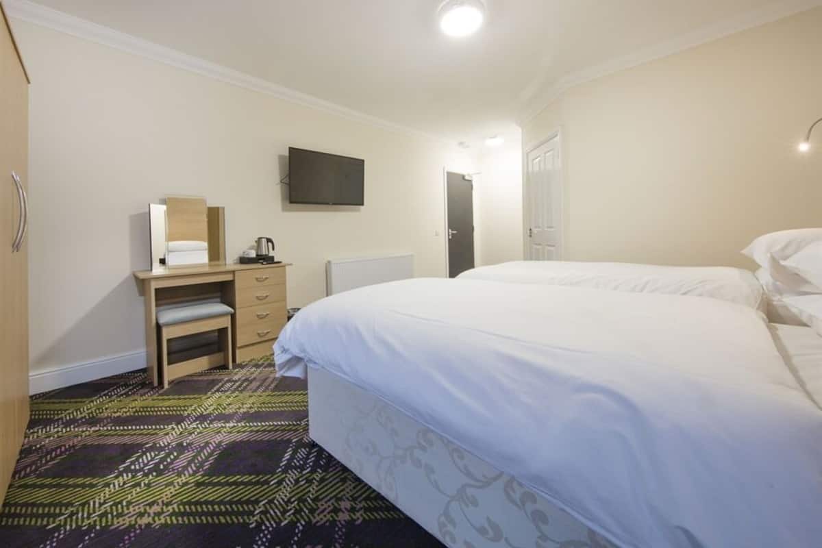 A hotel room with a bed, a desk with a chair, a television mounted on the wall, and a door leading to another room.