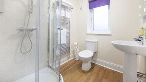 A bathroom with a glass shower enclosure, a white toilet, and a sink with a purple window blind. - The Bay Horse (Hamilton)