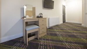 A hotel room with a wooden desk, a mirror, a television mounted on the wall, and a patterned carpet. - The Bay Horse (Hamilton)