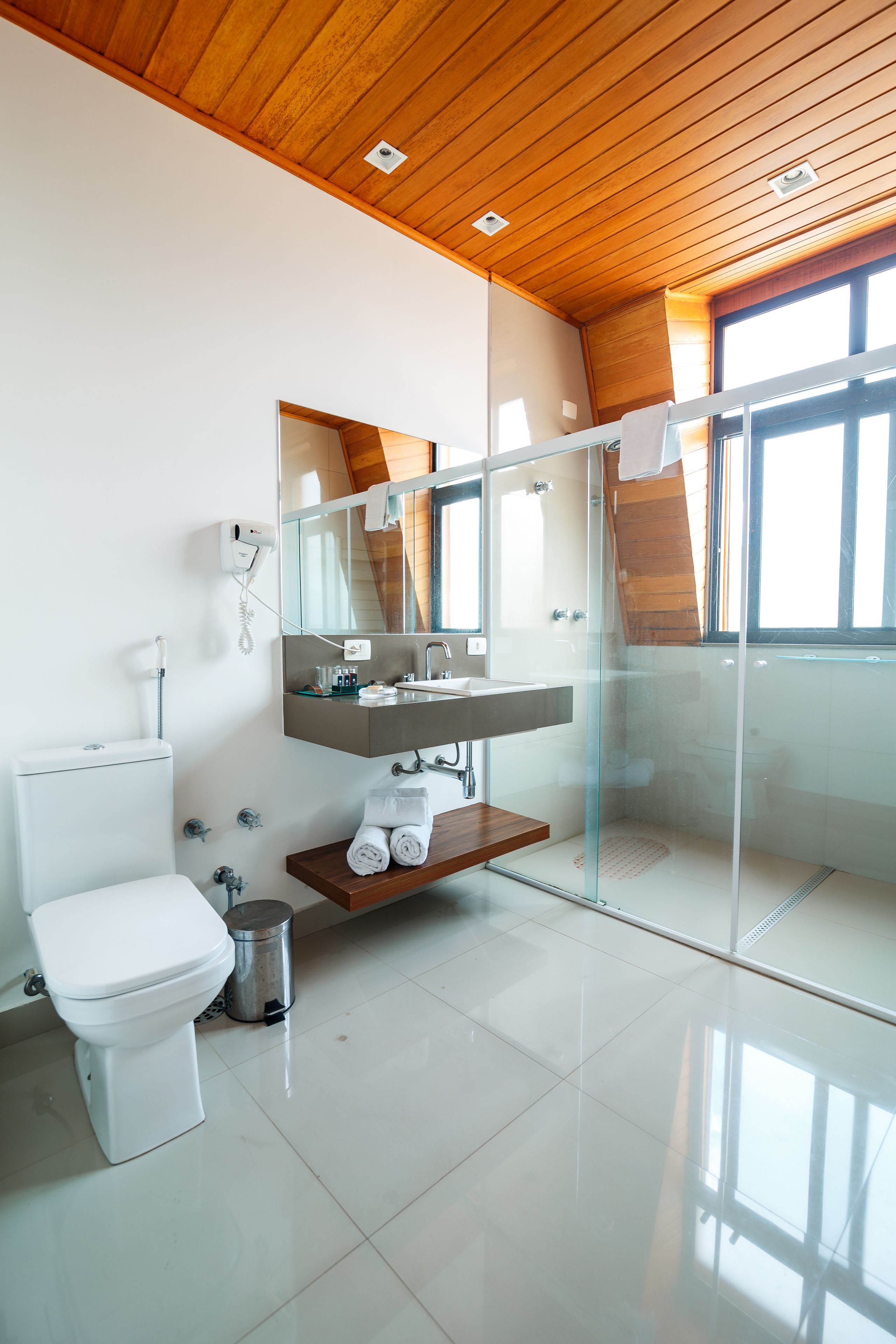 Une salle de bain moderne avec une douche à parois de verre, des toilettes, un lavabo avec un miroir et une étagère en bois.