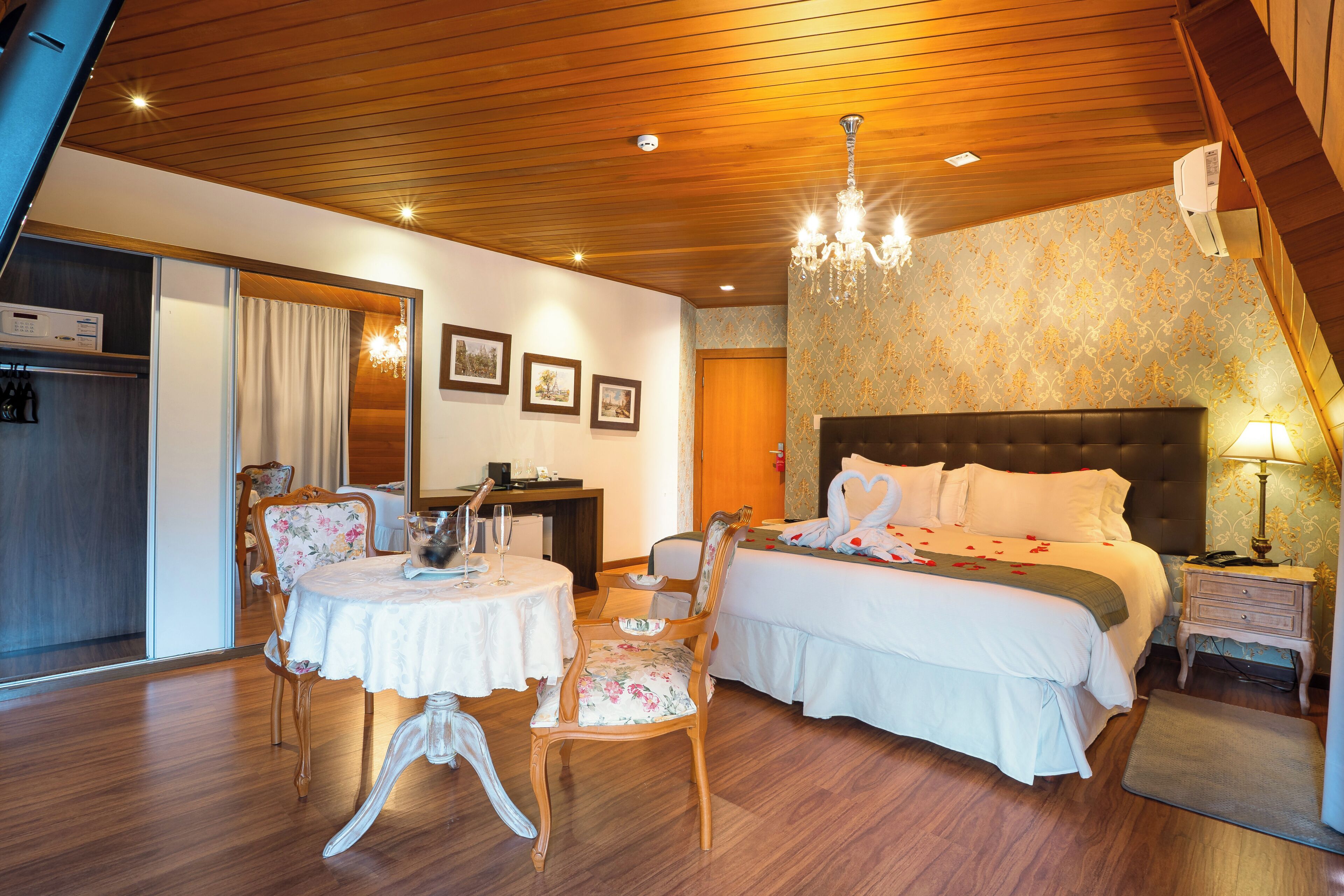 Ein Hotelzimmer mit einem Bett, einem Esstisch mit Stühlen, einer Kandelaber und einem Schreibtisch mit Computer.