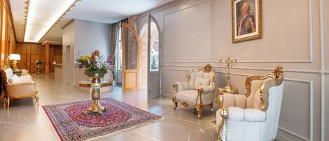 A luxurious lobby with marble floors, ornate chairs, and a large red and blue rug.