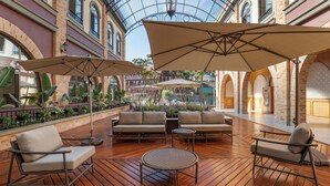 Um pátio interno com piso de madeira, assentos acolchoados e grandes guarda-sóis.