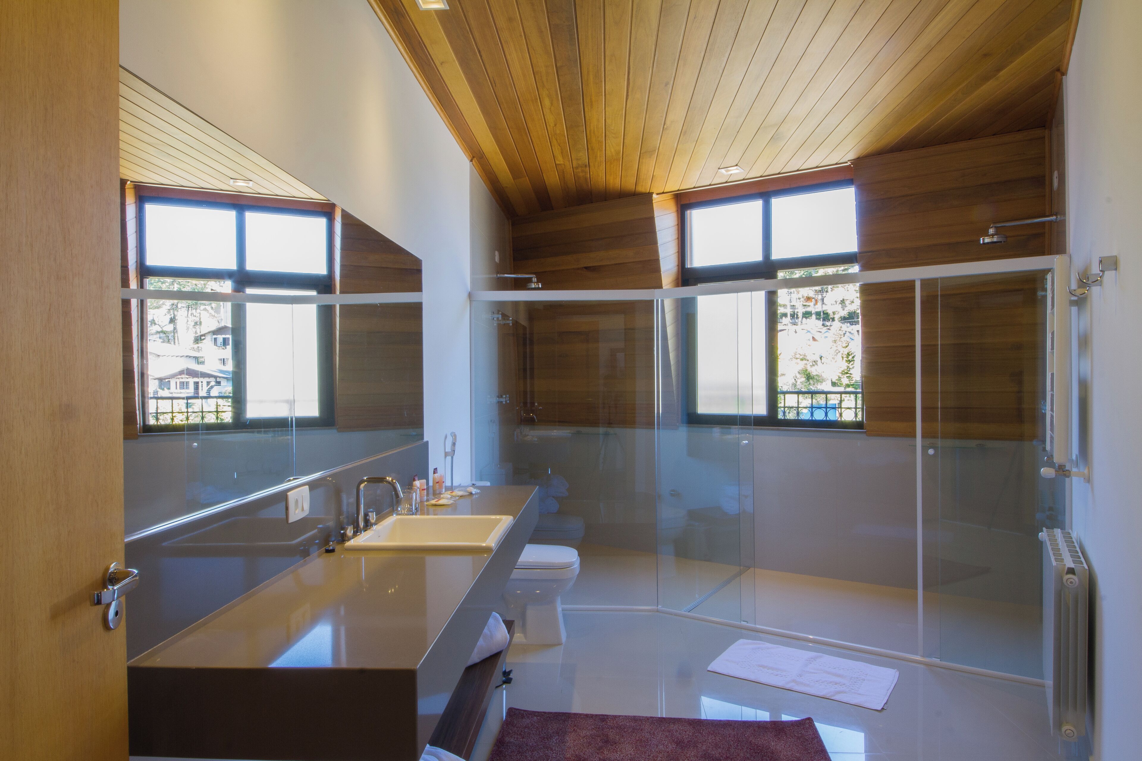 A modern bathroom with a glass shower enclosure, a large mirror, and a wooden ceiling.