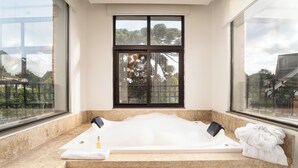 Um quarto de spa com uma banheira grande, uma janela com vista para árvores e uma toalha ao lado.