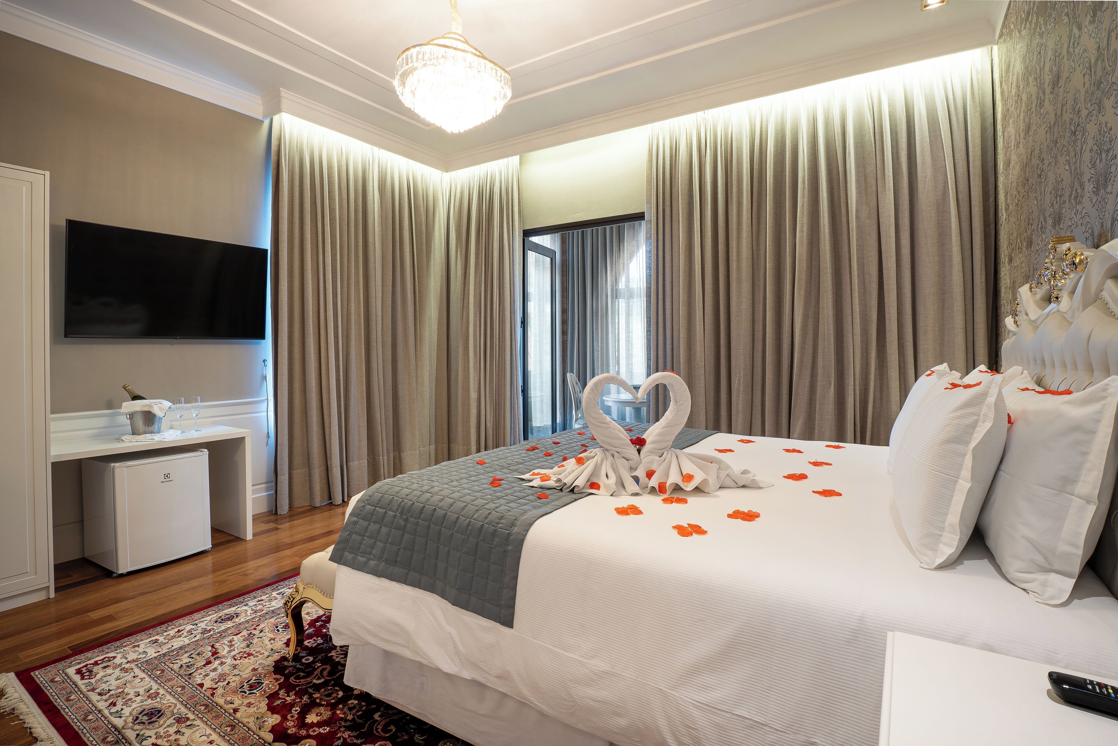 A hotel room with a large bed, a flat-screen TV, a small desk, and a chandelier.