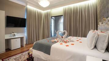 A hotel room with a large bed, a flat-screen TV, a small desk, and a chandelier.
