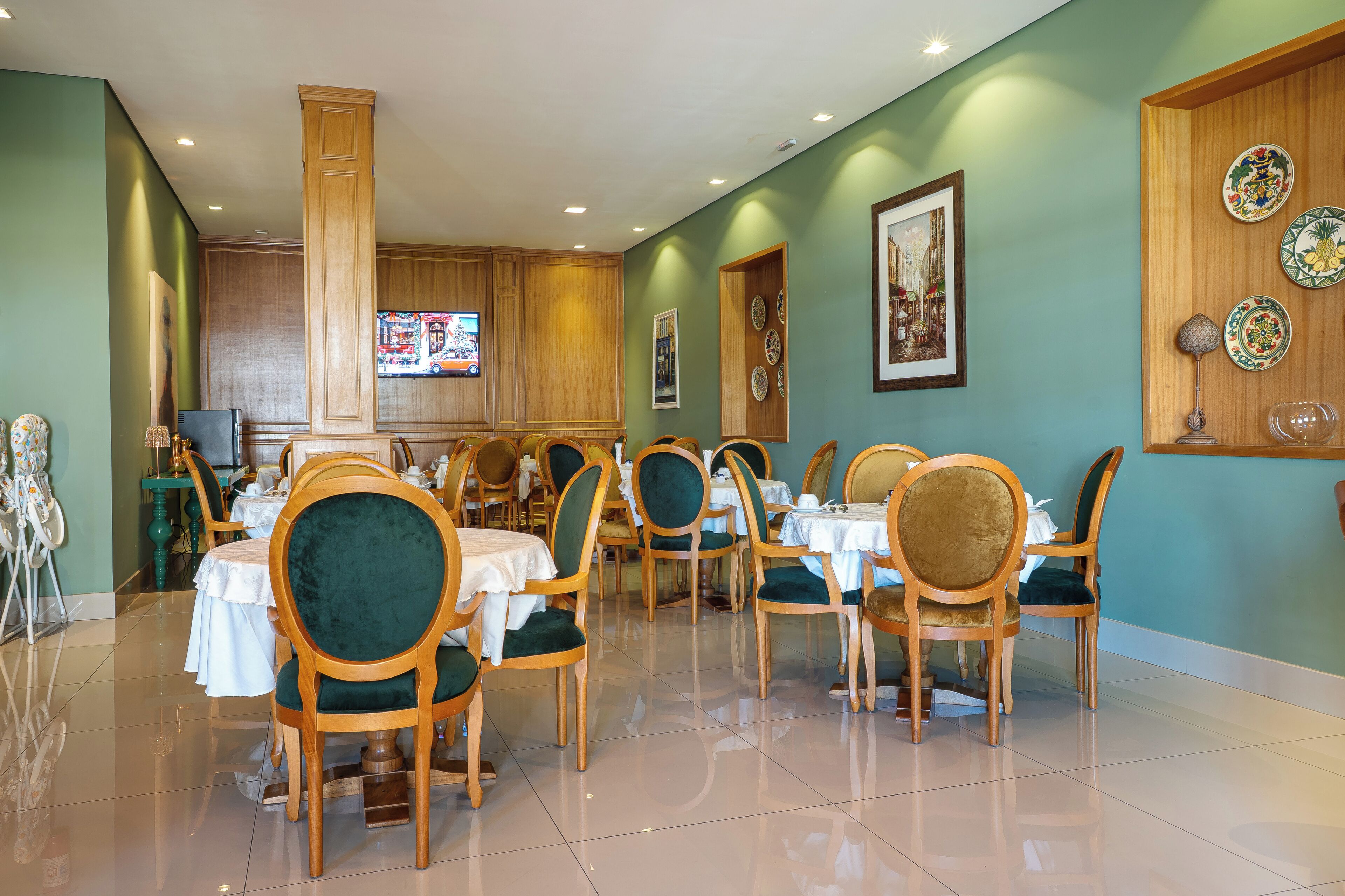 Un comedor con sillas y mesas de madera, un televisor y platos decorativos colgados en la pared.